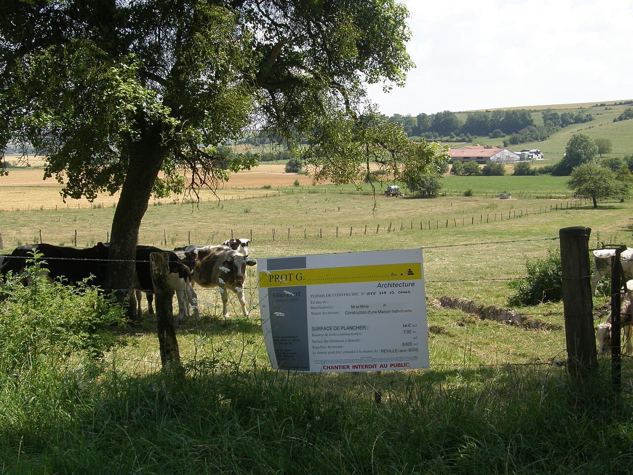 Panneau d'affichage de permis de construire installé sur un terrain en bordure de prairie