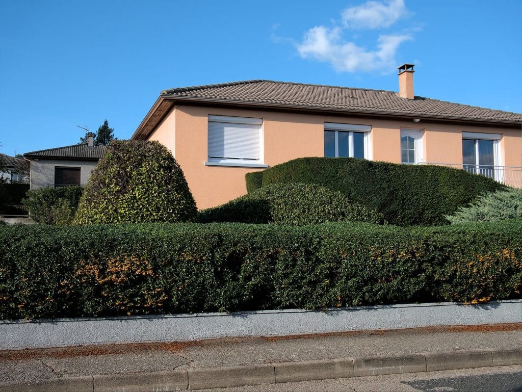 Pavillon aux volets blancs entouré de haies taillées en boules et en arrondi
